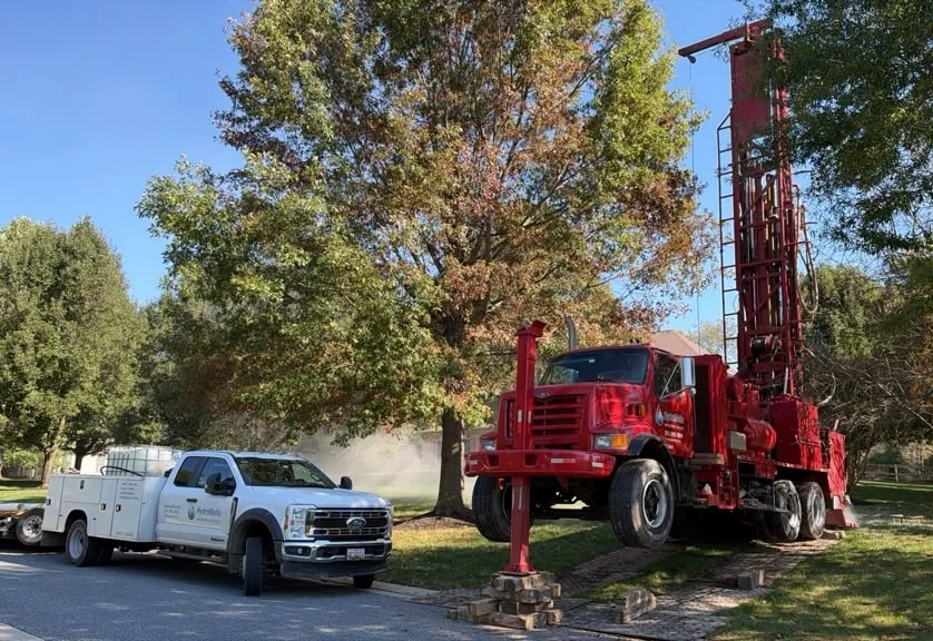 HydroWells service truck and red drill rig set up on a residential lawn with the mast raised