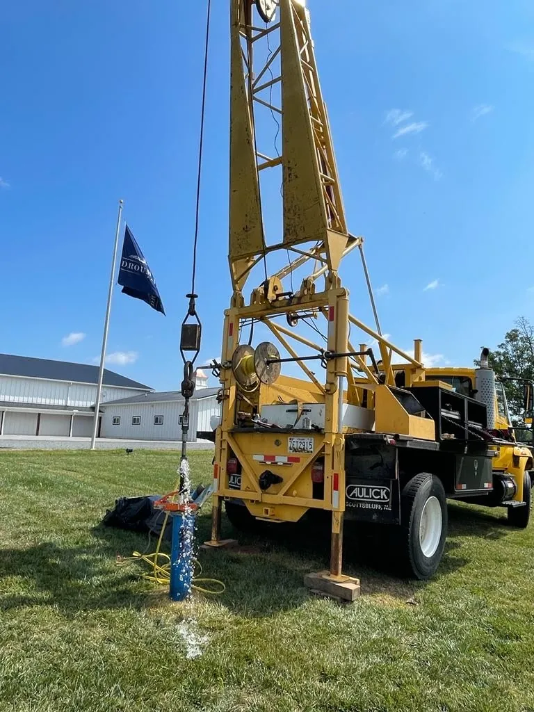 Water flowing from a new well casing under the HydroWells drill rig