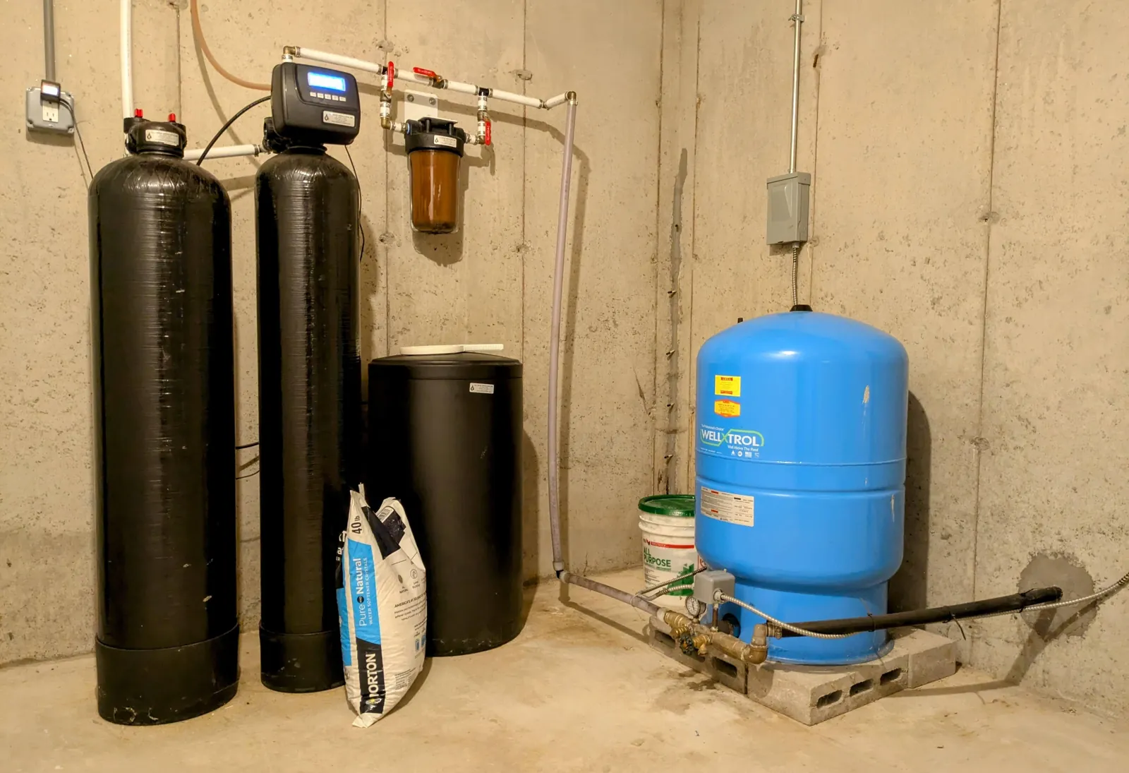 Water softener resin tanks and a brine tank beside a sediment filter and a blue well pressure tank in a basement